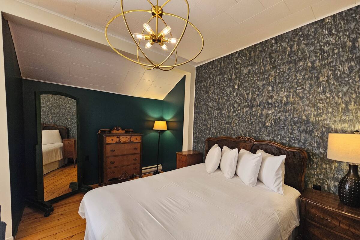 A bedroom with a large bed, a dresser, a nightstand, a lamp, and a mirror.