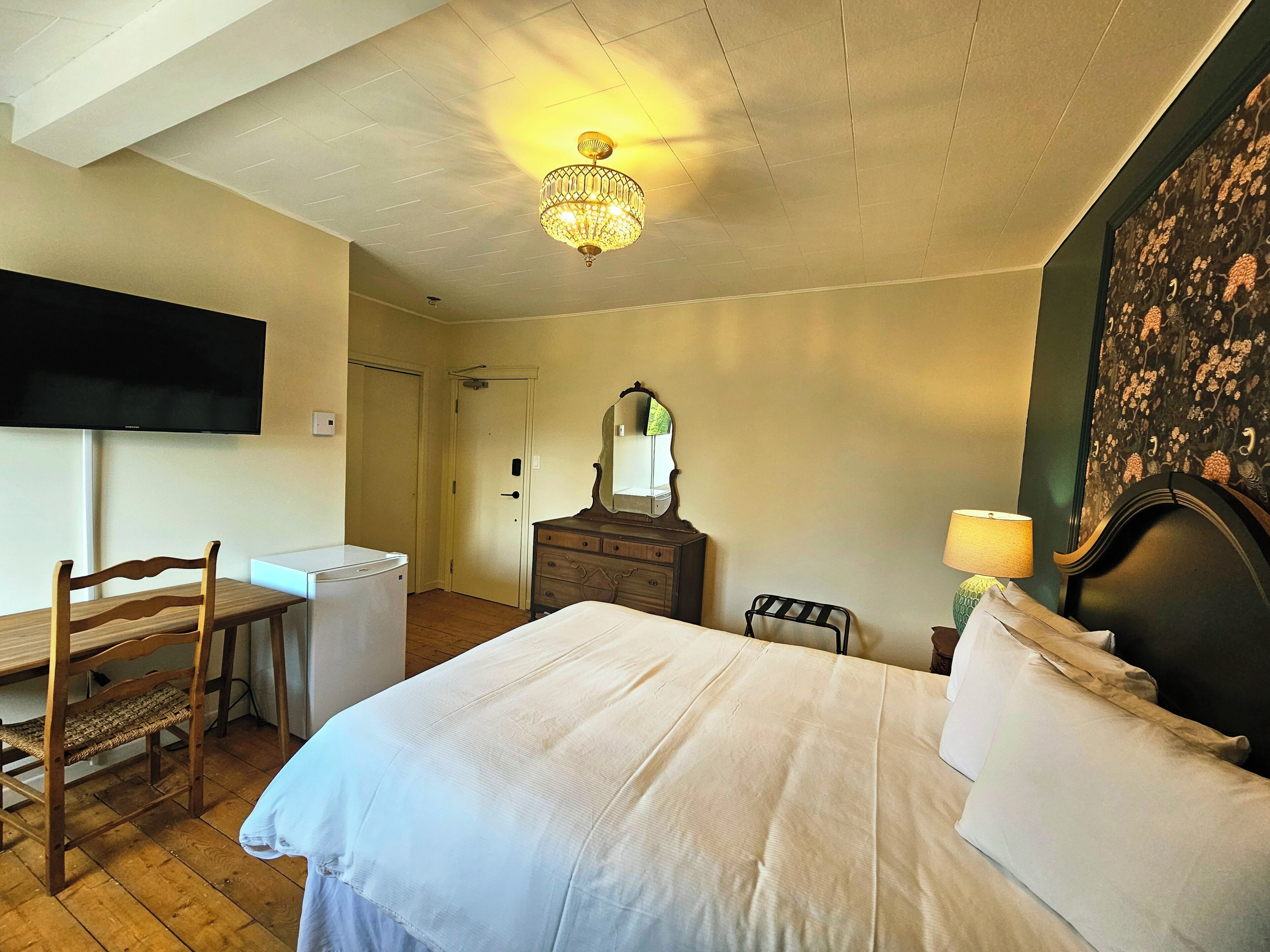 Quarto com cama, cômoda, cadeira, escrivaninha, televisão e lustre.