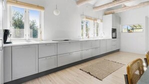 Eine moderne Küche mit einer langen Arbeitsplatte, weißen Schränken und Holzbalken an der Decke.