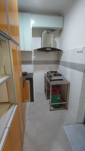 A compact kitchen with a gas stove, a small table, and a red gas cylinder.