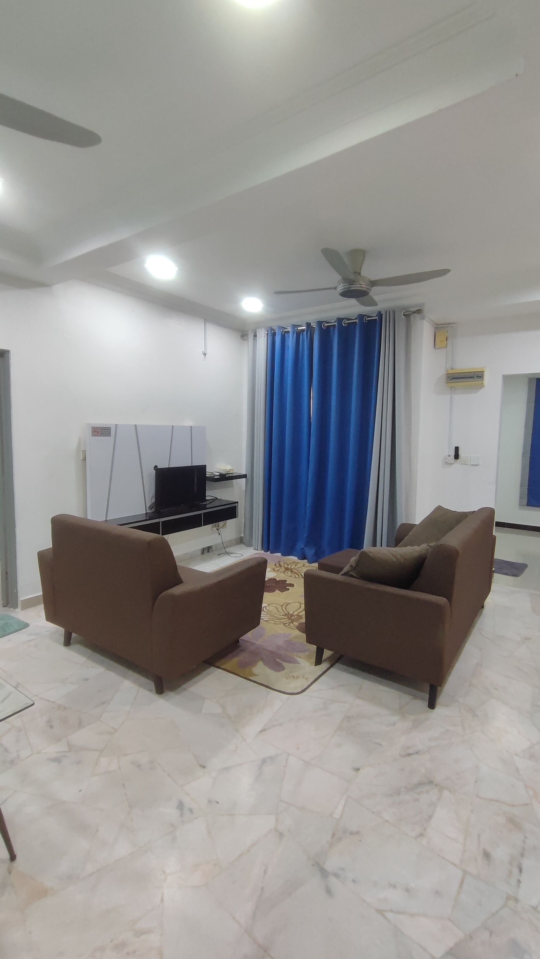 Un salon avec deux canapés marron, un ventilateur de plafond, un téléviseur à écran plat et un rideau bleu.