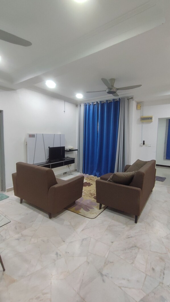 A living room with two brown sofas, a ceiling fan, a flat-screen TV, and a blue curtain.