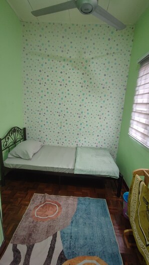 Una habitación pequeña con una cama, un ventilador de techo, una pared con lunares, piso de madera y una ventana con persianas.