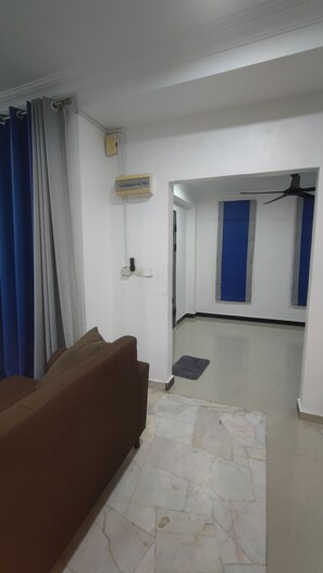 Una habitación con un sofá marrón, un radiador, un ventilador de techo y una persiana azul.