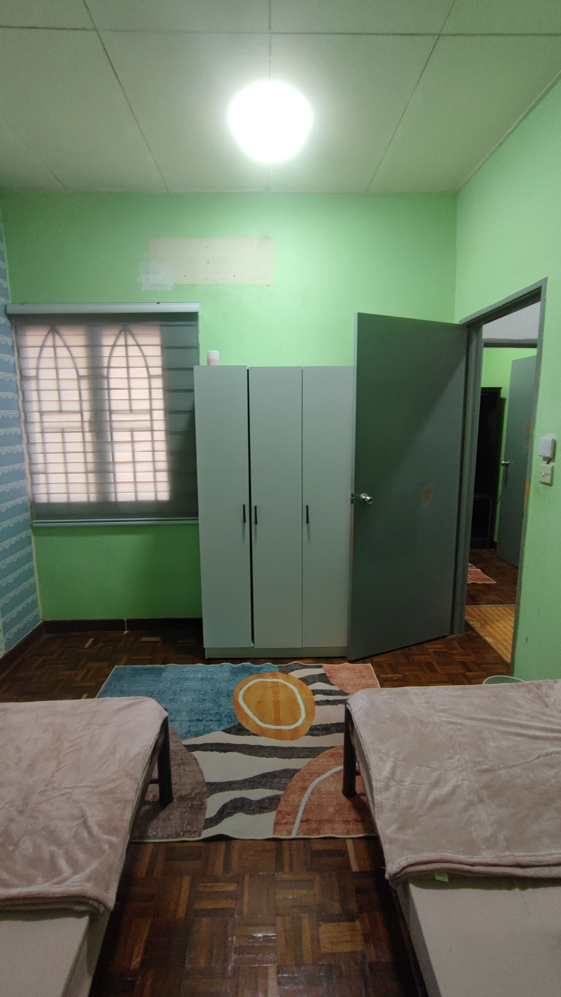 A room with two beds, a wardrobe, a window with blinds, and a carpet.