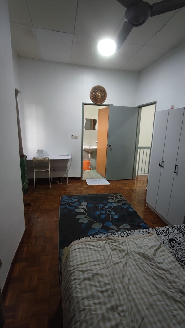 A bedroom with a bed, a desk, a chair, a wardrobe, and a bathroom visible through an open door.