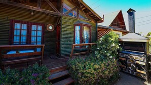 Une cabane rustique en rondins de bois, dotée d’un porche, de bancs en bois et d’une cheminée en pierre.