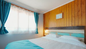 Un lit avec une tête de lit en bois, une fenêtre avec des rideaux et un tableau accroché au mur.
