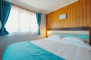 Un lit avec une tête de lit en bois, une fenêtre avec des rideaux et un tableau accroché au mur.