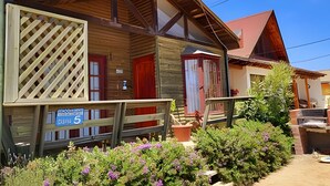 Un bâtiment en bois doté d’un balcon, d’une enseigne indiquant le numéro de chambre 5, et d’un jardin où poussent des fleurs violettes.