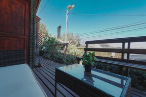 Une terrasse en bois avec une table et une chaise en verre, un pot de fleurs et une vue sur un immeuble et des lignes électriques.