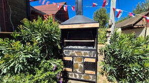 Un barbecue en pierre doté d’une cheminée, entouré de verdure et délimité par une clôture en bois.