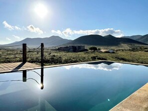 A clear pool with a wooden deck, surrounded by a natural landscape with mountains in the background. - Cortijo with eclectic décor near Almería (Albaricoques)