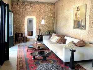 A room with a stone wall, a white sofa, a patterned rug, a guitar, and a painting. - Cortijo with eclectic décor near Almería (Albaricoques)