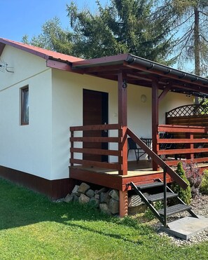 A small, single-story building with a wooden deck and a door. - Komfortowy domek nad Soliną z widokiem. Taras, grill, zwierzęta mile widziane! (Zawóz)