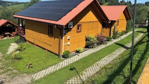 A wooden cabin with a red roof, solar panels, and a paved pathway leading to a picnic area.