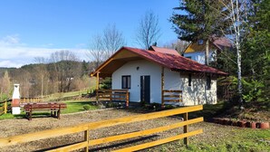 A small white building with a red roof, a wooden fence, and a bench in a rural setting.