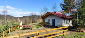 A small white building with a red roof, a wooden fence, and a bench in a rural setting. - Komfortowy domek nad Soliną z widokiem. Taras, grill, zwierzęta mile widziane! (Zawóz)