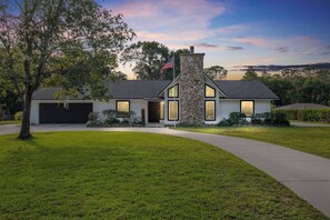 A modern two-story house with a stone chimney, a garage, and a well-maintained lawn. - Horsey Heartland oasis 7 Mi WEC Close to all Fun (Ocala)