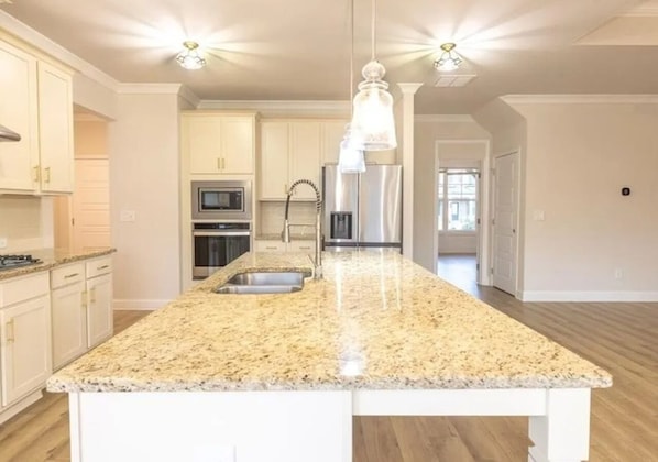 A kitchen with granite countertops, stainless steel appliances, and pendant lighting.