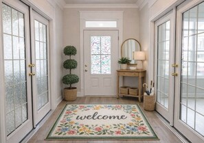 A hallway with a welcome mat, a potted plant, a mirror, and wicker baskets.