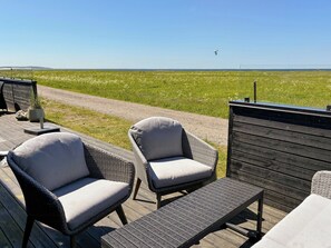 Une terrasse dotée de chaises et d’une table en osier, offrant une vue sur un champ verdoyant et un ciel dégagé.