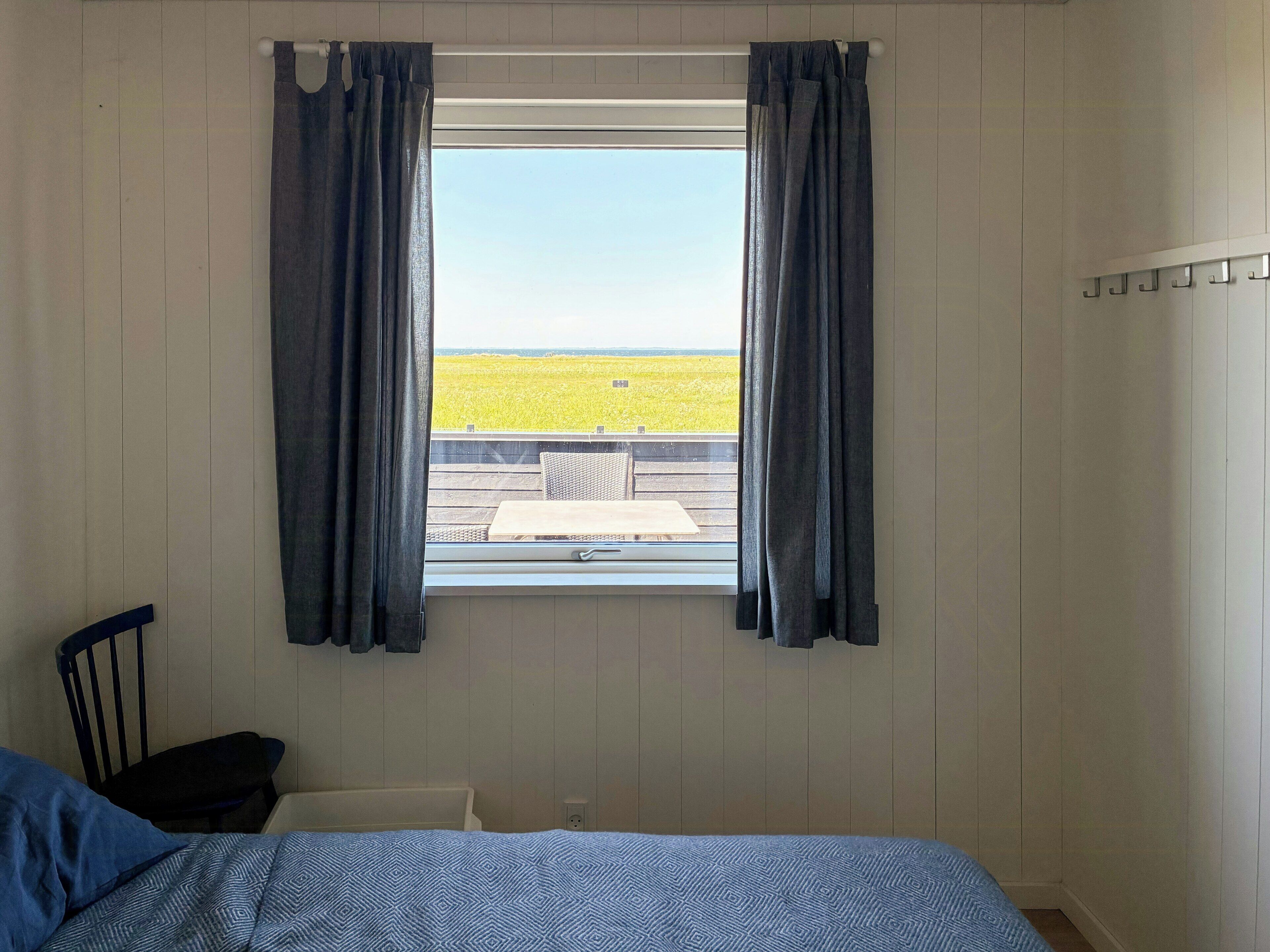 Une pièce avec un lit, une chaise, une fenêtre avec des rideaux et une vue sur un champ.