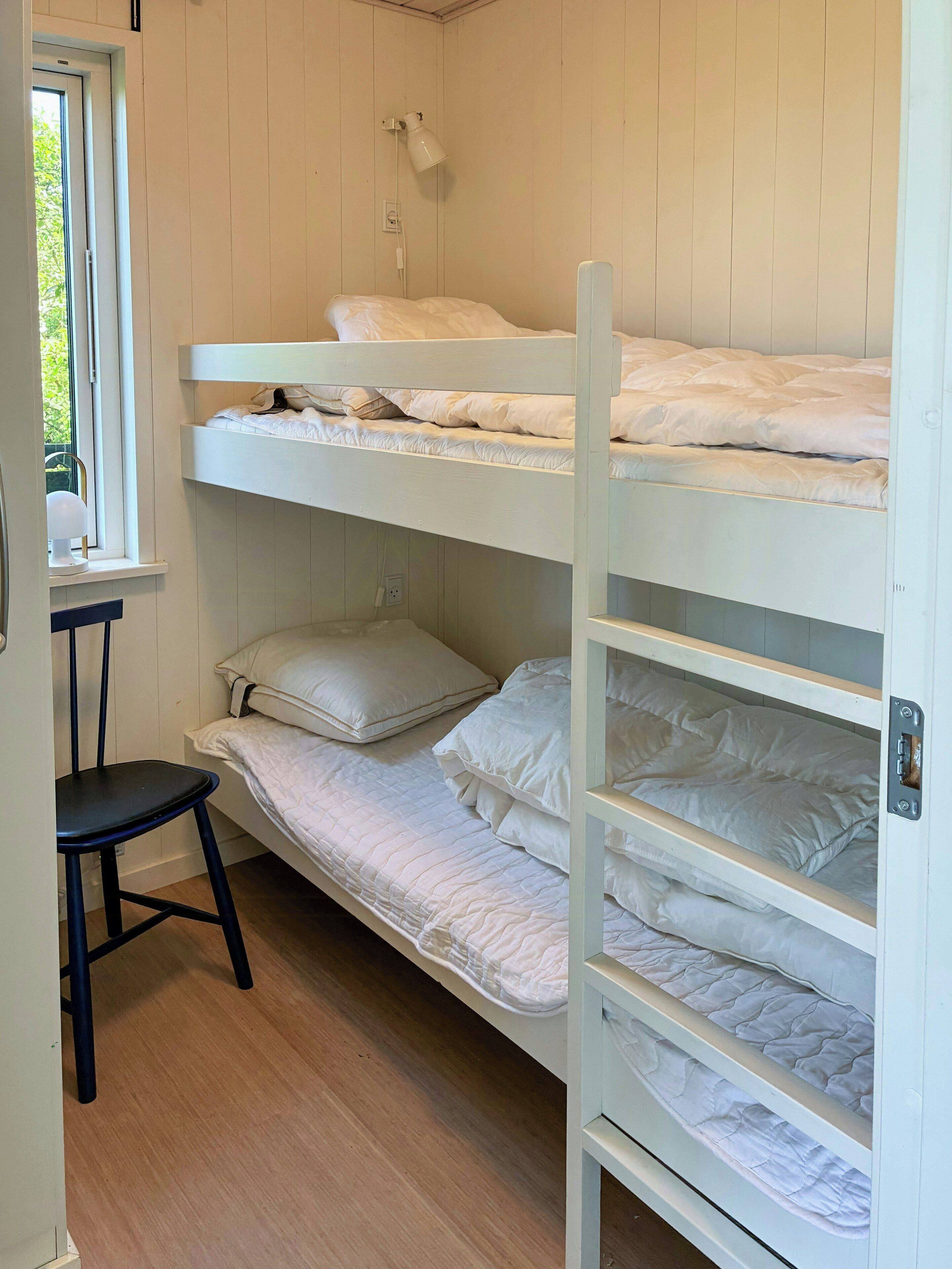A bunk bed room with a chair, a window, and a wall-mounted lamp.