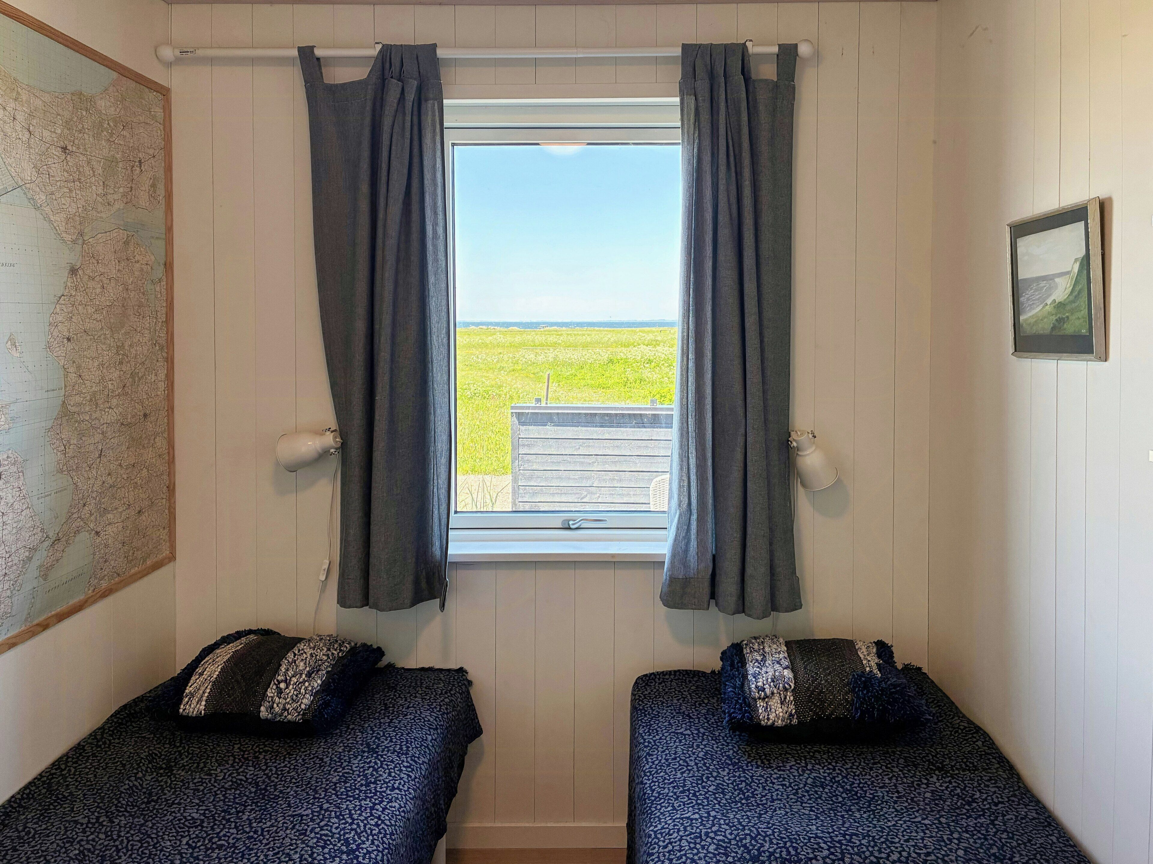 Una habitación con dos camas, una ventana con cortinas, un mapa en la pared y un cuadro.