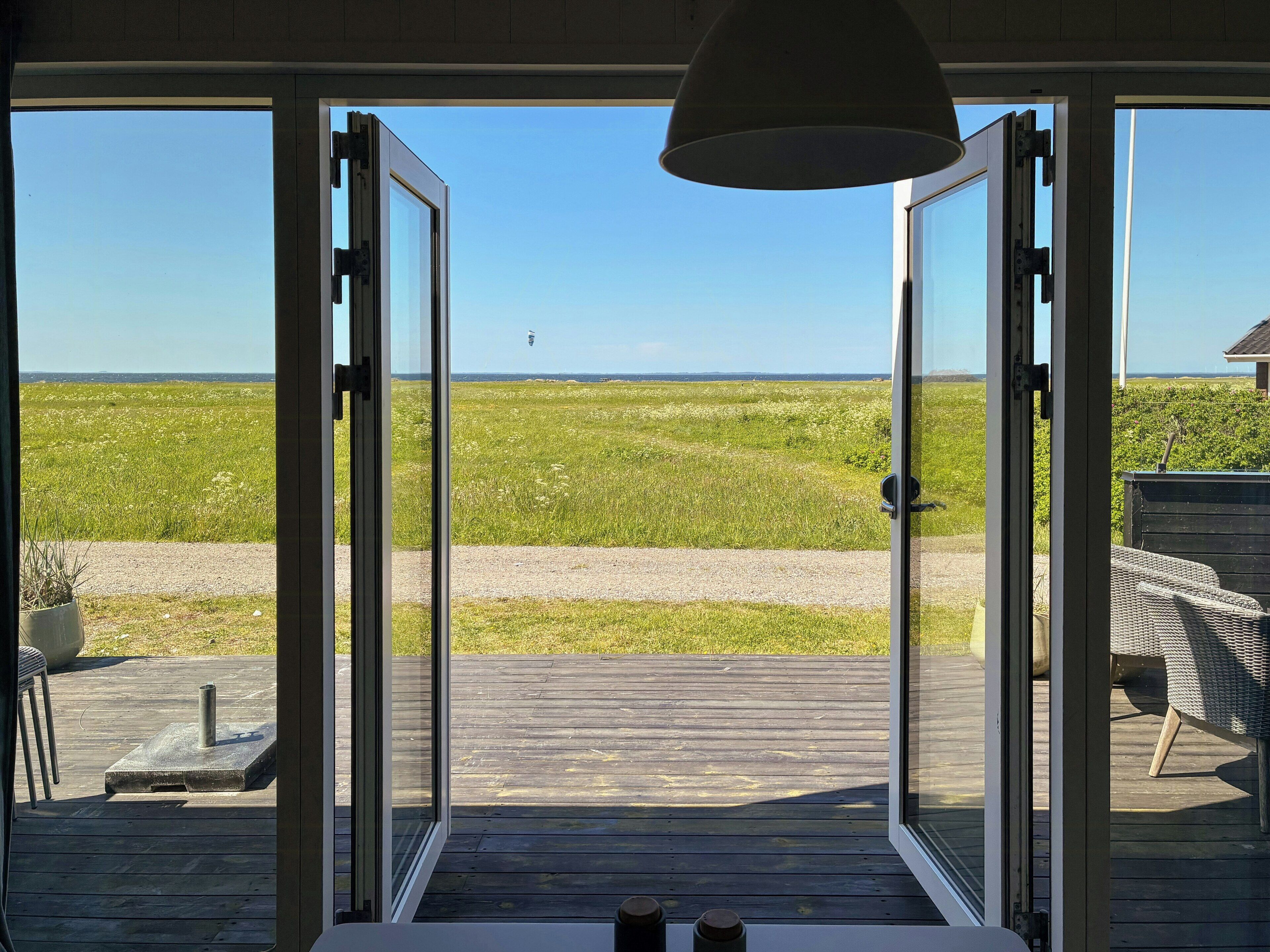 A room with a large glass door leading to a wooden deck overlooking a grassy field.. Fjord Views and a Child‑Friendly Beach in Lendrup