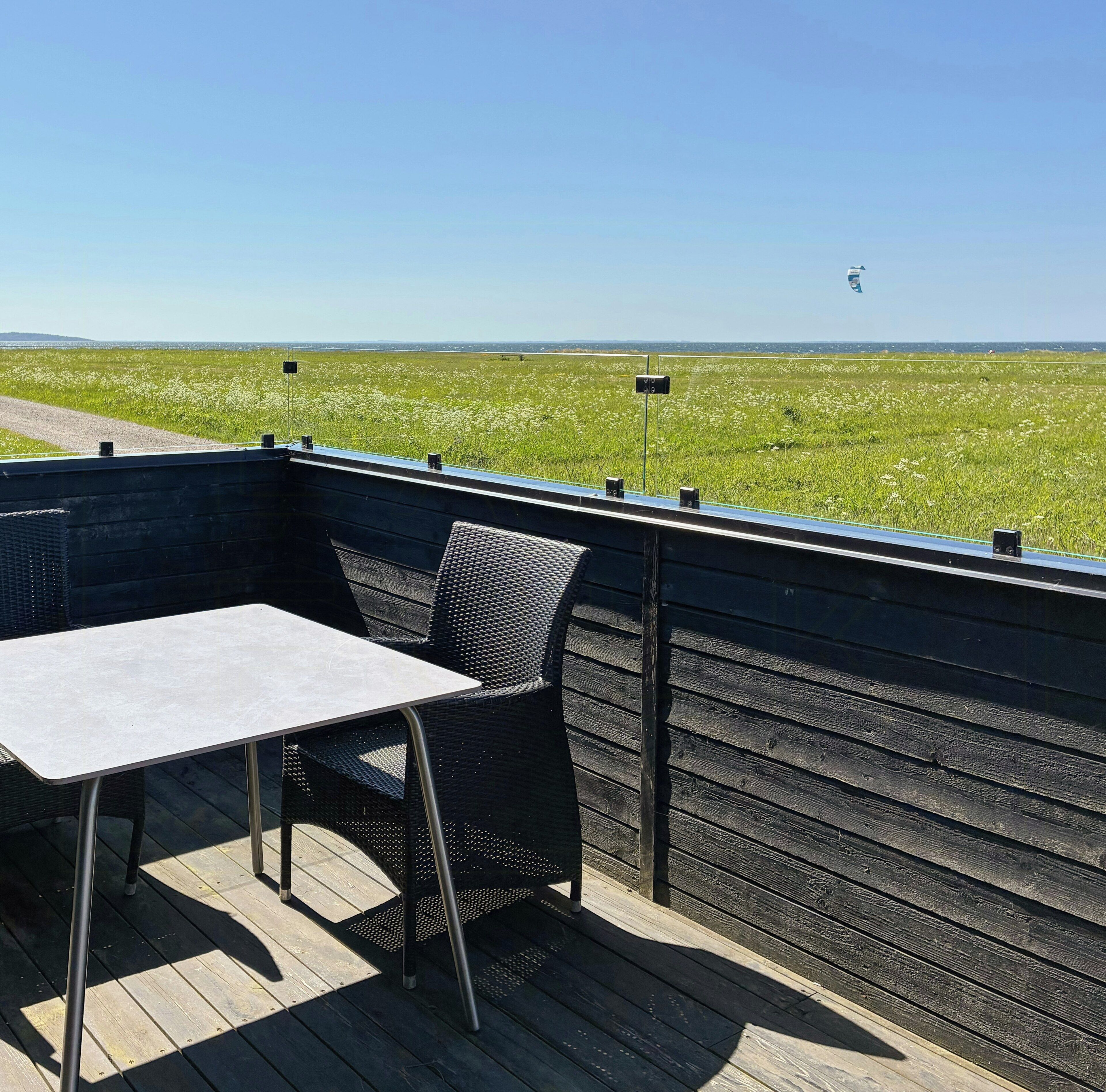 A deck with a table and chairs, overlooking a field with a clear sky.