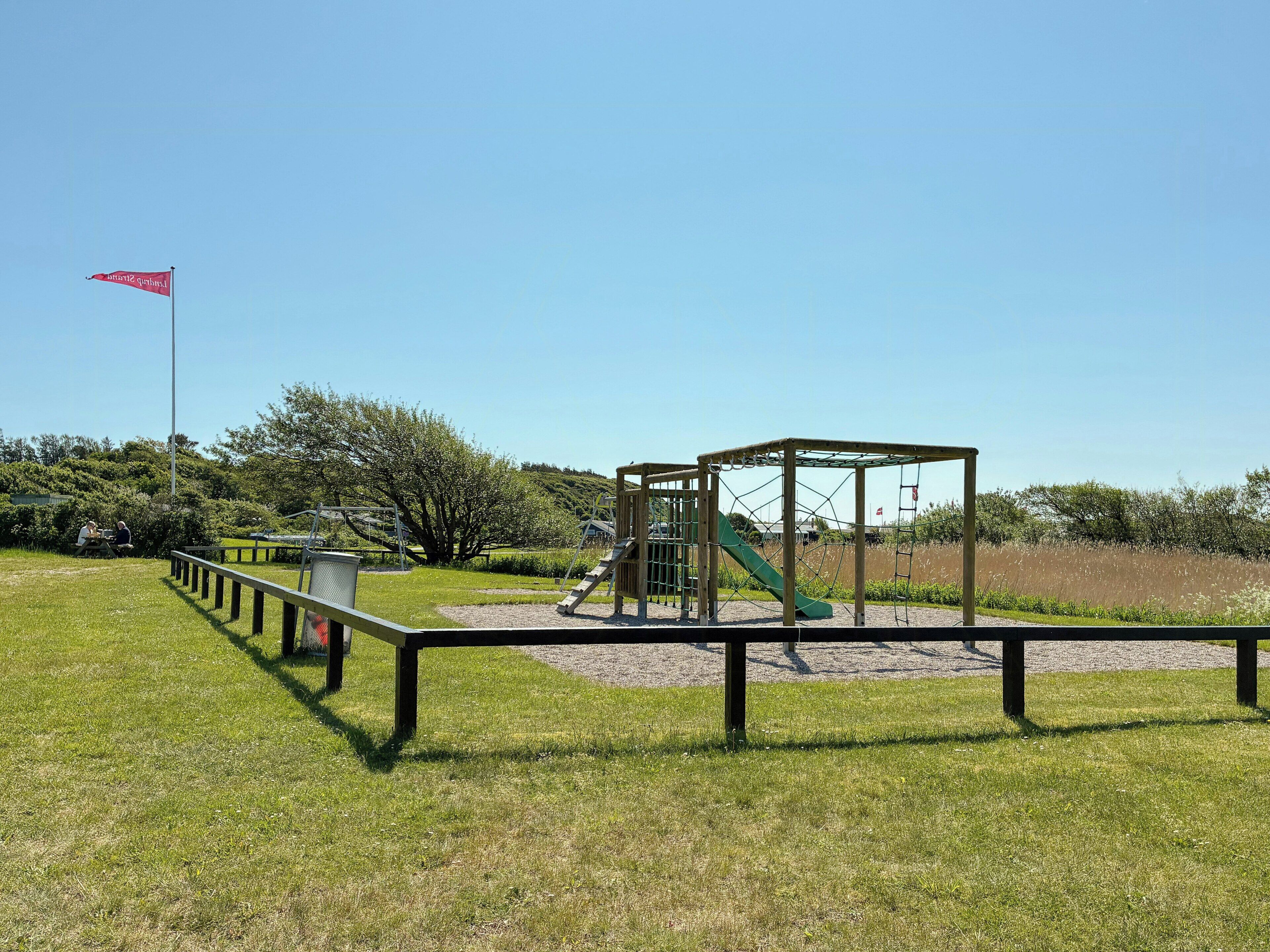 Ein Spielplatz mit Rutsche und Klettergeräten, umgeben von Rasenflächen und Bäumen.