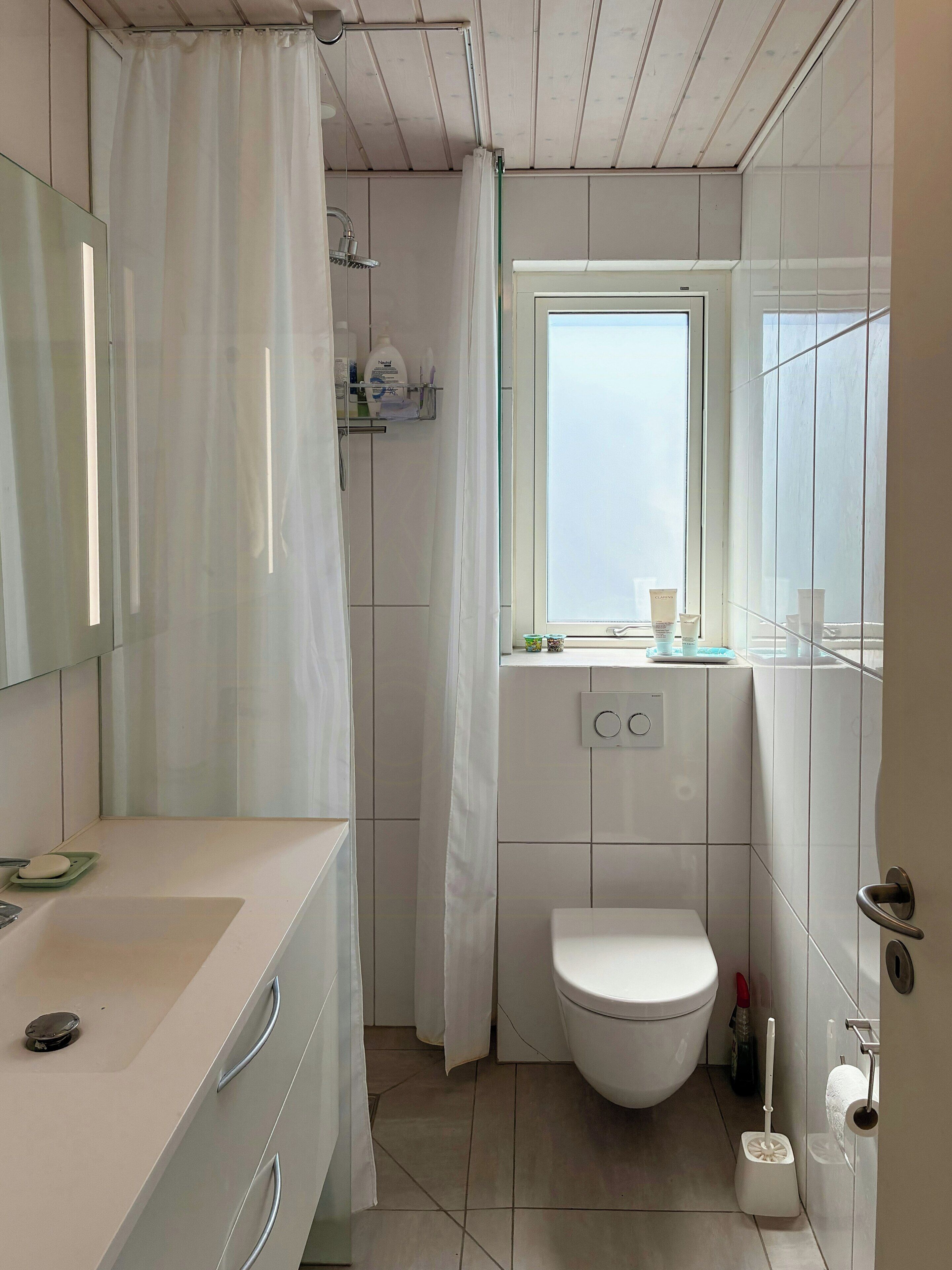 A bathroom with a shower, toilet, sink, and a window.