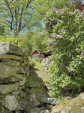 Un muro de piedra, un edificio rojo y un árbol con flores moradas.