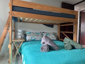 Ein Etagenbett mit Holzrahmen, einer türkisblauen Bettdecke und einem Kissen mit geometrischem Muster.