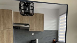 Uma cozinha moderna com armários de madeira, bancada de mármore, dois bancos altos brancos e uma luminária pendente preta.