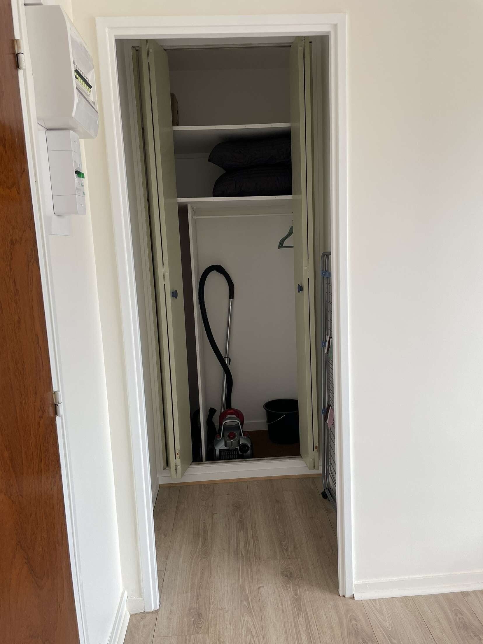 A hallway leading to a closet with a vacuum cleaner and a bucket.