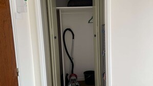 Corredor que dá para um armário com um aspirador de pó e um balde.