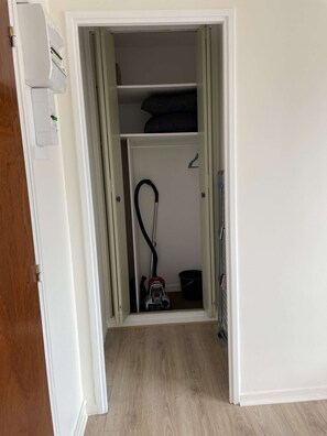 Un couloir menant Ă un placard oĂč se trouvent un aspirateur et un seau.