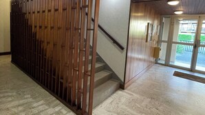 Um corredor com divisória de madeira, escada e vista para o exterior através de portas de vidro.