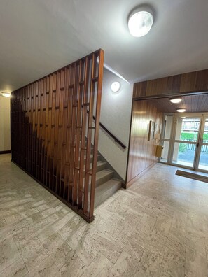 Un couloir avec une cloison en bois, un escalier et une vue sur lâextĂ©rieur Ă travers des portes vitrĂ©es.