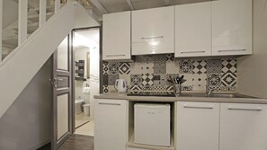 Uma cozinha compacta com armários brancos, uma geladeira pequena e um painel de cozinha padronizado.