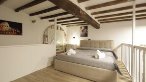 Quarto com cama, espelho redondo, pintura do Coliseu e vigamento de madeira.
