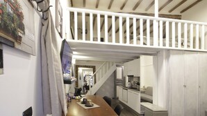 A loft-style room with a wooden ceiling, a dining area with a table and chairs, a kitchen with white cabinets, and a staircase leading to an upper level. - Coppelle Nights at the Pantheon (Roma)