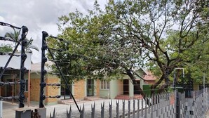 Un área cercada con valla metálica, árboles y edificios al fondo.