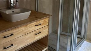 Un baño con tocador de madera, lavamanos y cabina de ducha con mampara de vidrio.