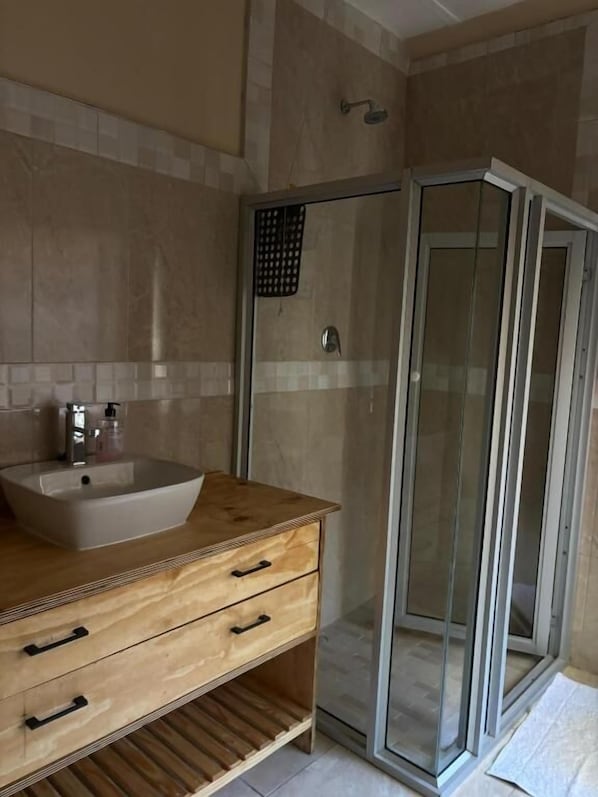 A bathroom with a wooden vanity, a sink, and a glass shower enclosure. - Laroza Guest House (Rustenburg)