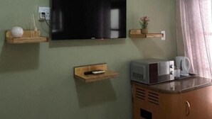 Una habitación con un televisor montado en la pared, un microondas en la encimera y un mueble pequeño.