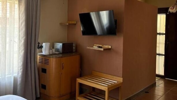 Habitación de hotel con cama, un banco de madera, televisor montado en la pared, ventilador de techo y un minibar.