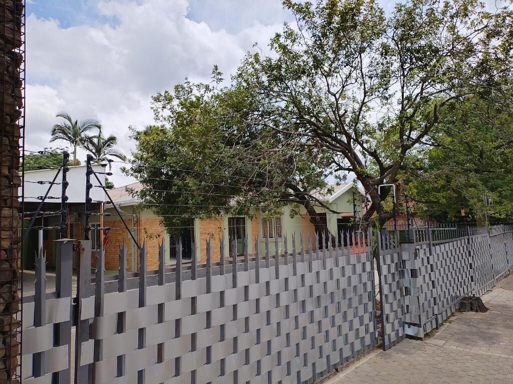 A grey metal fence with a lattice design, a paved walkway, and a building with multiple windows in the background.